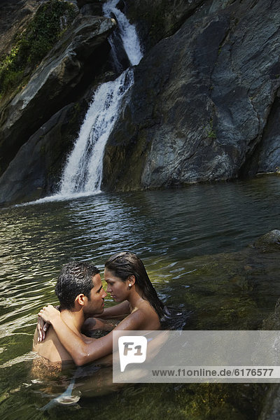 Hispanic couple hugging in water