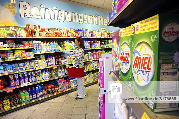 Woman looking at cleaning products in a corridor with household goods while shopping in a self-service grocery department  supermarket  Germany  Europe