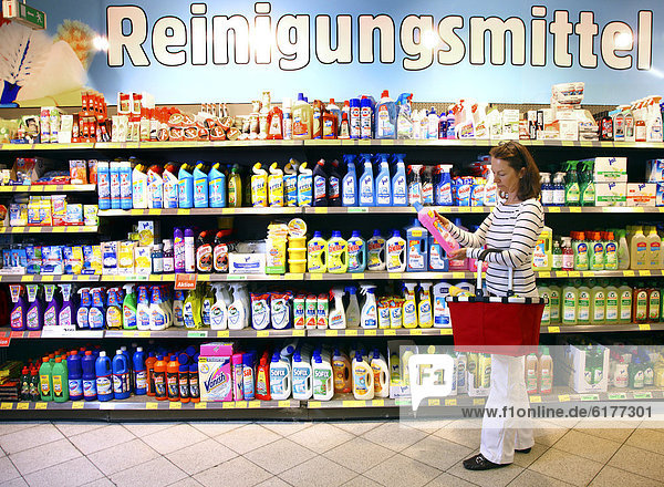 Woman looking at cleaning products in a corridor with household goods while shopping in a self-service grocery department  supermarket  Germany  Europe