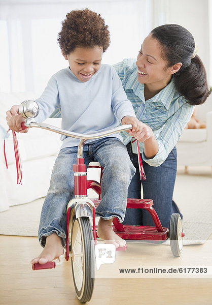Mixed race woman teaching son to ride tricycle