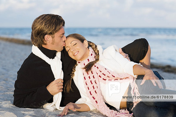 Hispanic couple sitting on beach