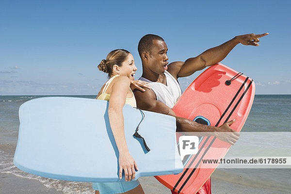 Multi-ethnic couple holding bodyboards