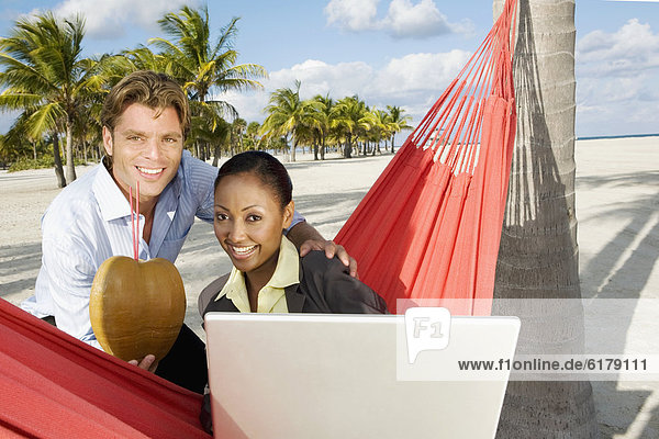 Hispanic couple with laptop and tropical cocktail
