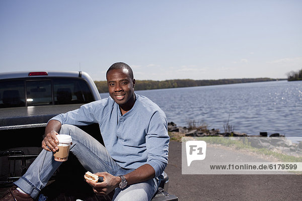 Black man sitting in truck bed eating lunch