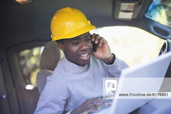 Black man wearing hard hat in vehicle using laptop