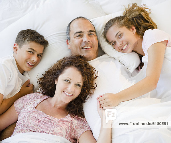 Smiling Hispanic family laying in bed together