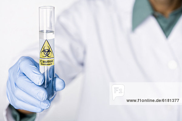 Hispanic scientist holding test tube with caution sticker full of water