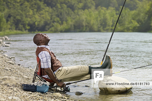 Black man with feet up fishing in stream