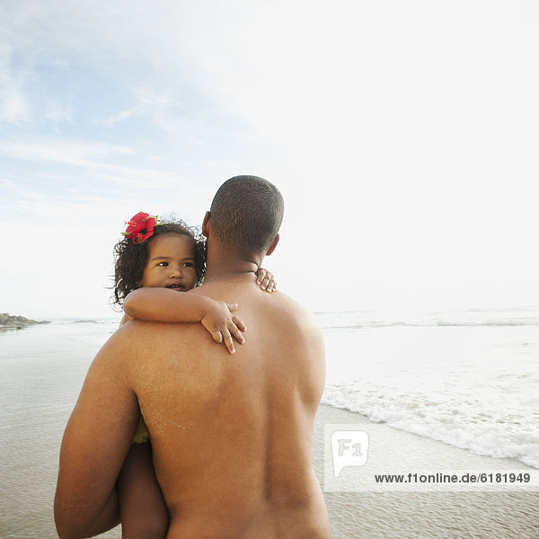 Black father carrying daughter on beach
