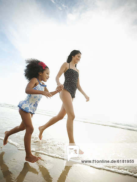 Hispanic mother and daughter holding hands and walking on beach