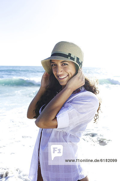 Smiling mixed race woman in hat on beach