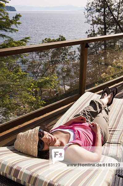 Hispanic woman laying on deck chair sunbathing