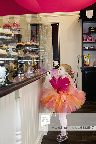 Caucasian girl in tutu looking at cupcakes in bakery