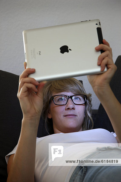 Junge Frau liegt auf einem Sofa und surft mit einem iPad Tablet-Computer drahtlos im Internet