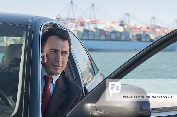 Hispanic businessman using cell phone in car with container ship in background