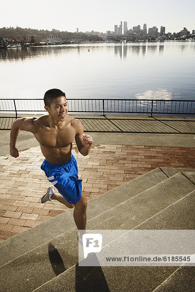 Bare chested Asian man jogging along urban waterfront