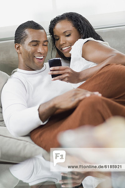 Multi-ethnic couple laying on sofa looking at cell phone