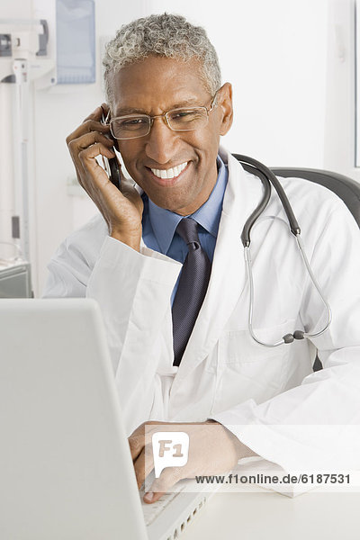 Mixed race doctor sitting at desk talking on cell phone