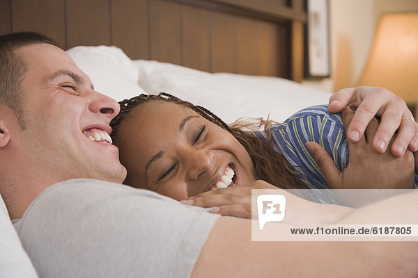 Multi-ethnic couple laughing in bed
