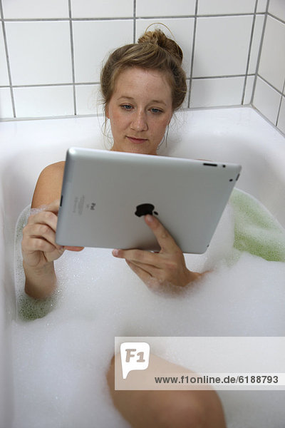 Junge Frau in der Badewanne mit einem iPad Tablet-Computer drahtloser Internet-Zugang