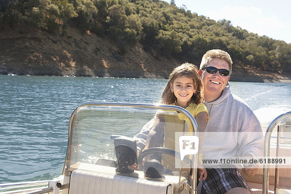 Father and daughter steering boat on lake