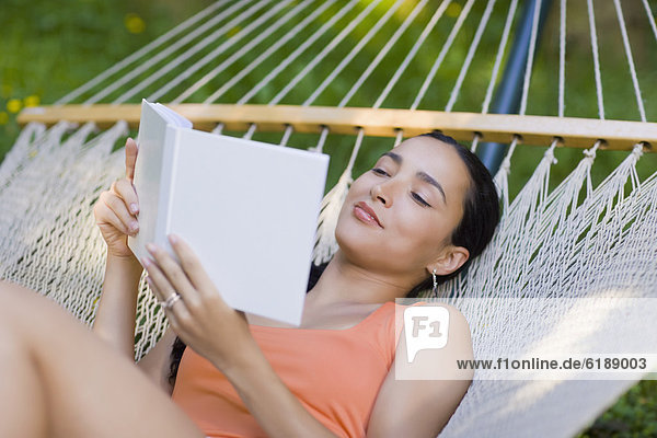 Hispanic woman laying in hammock reading