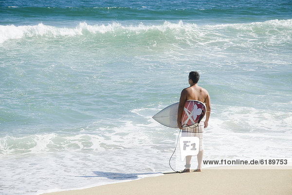Hispanic teenager at beach with surfboard