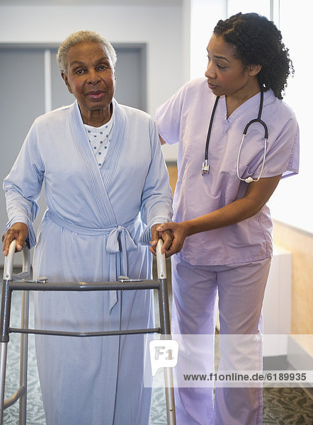 Nurse helping woman use walker in hospital hallway