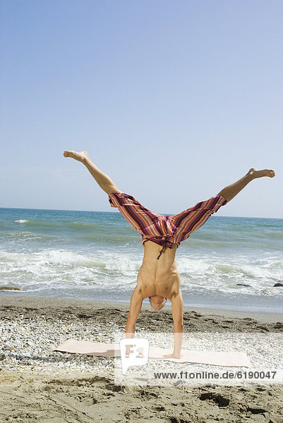 Hispanic man doing handstand on beach