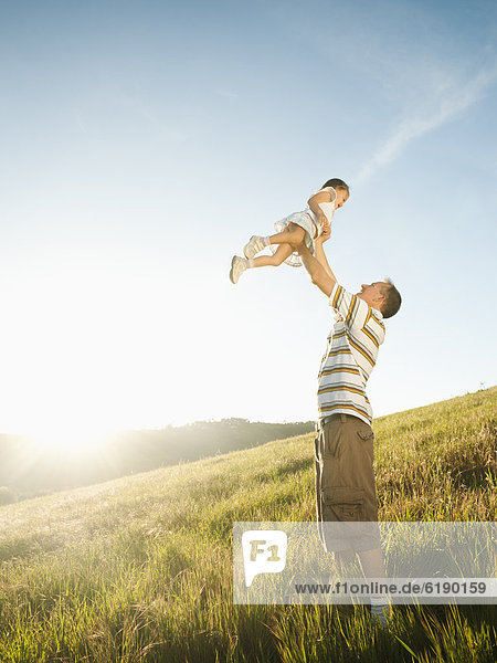 Father standing in field lifting daughter