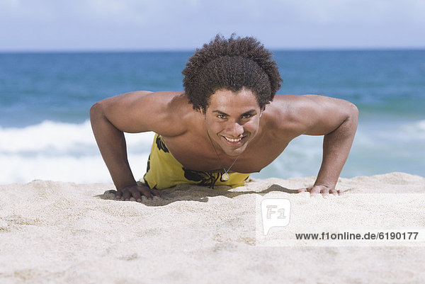 African man doing push-ups at beach