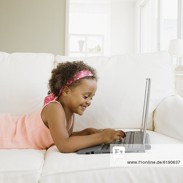 Mixed race girl typing on laptop in living room