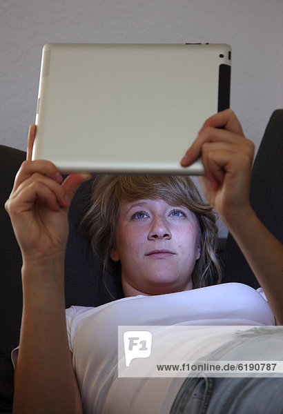 Junge Frau liegt auf Sofa und surft drahtlos im Internet mit einem iPad Tablet-Computer