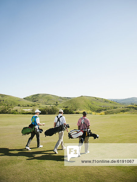 Männer tragen Golftaschen auf Golfplatz