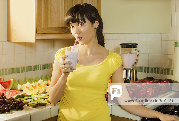 Mixed race woman drinking smoothie in kitchen