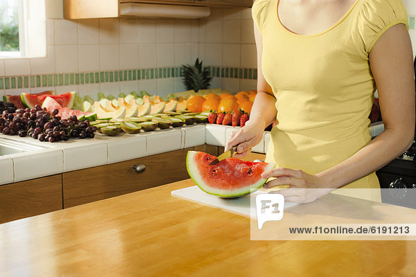 Mixed race woman cutting watermelon in kitchen