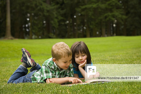 Brother and sister reading story book in park