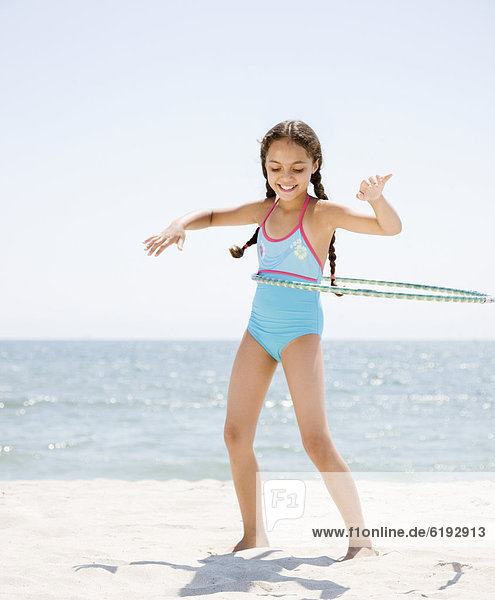 Hispanic girl playing with hula hoop on beach