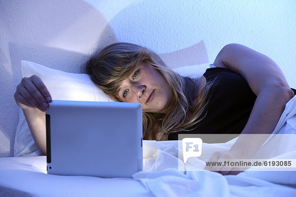 Junge Frau im Bett surft mit einem iPad Tablet-Computer per Drahtlosverbindung im Internet