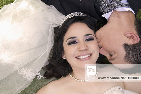 Hispanic bride and groom laying on ground