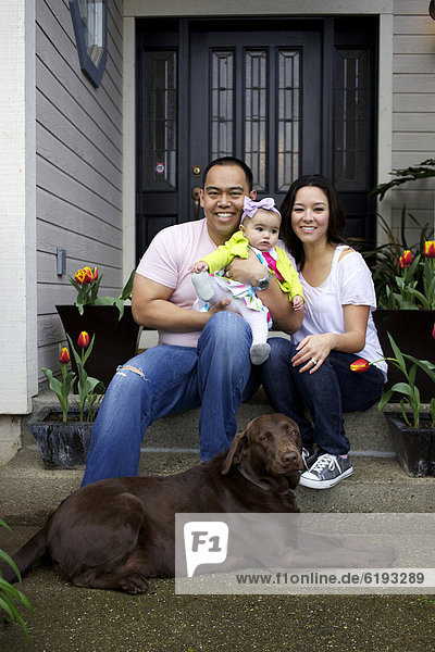 Mother and father sitting on front stoop with baby girl and dog