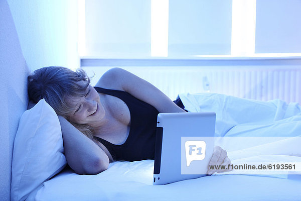 Junge Frau im Bett surft mit einem iPad Tablet-Computer per Drahtlosverbindung im Internet