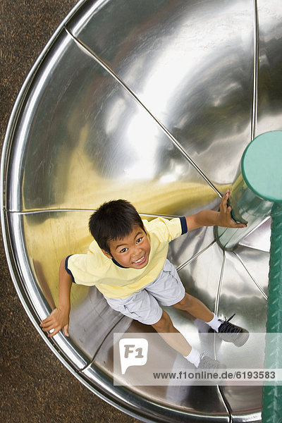 Asian boy sliding down circular slide