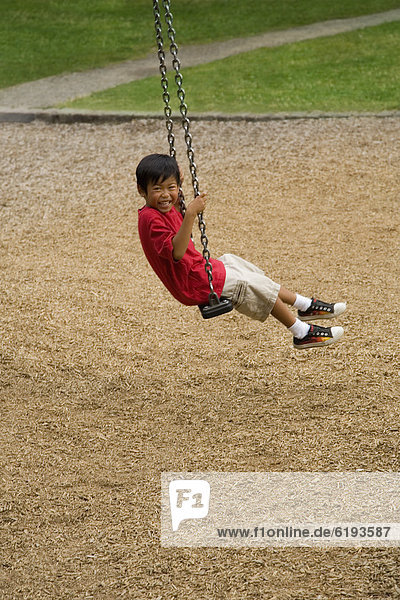 Asian boy swinging on playground
