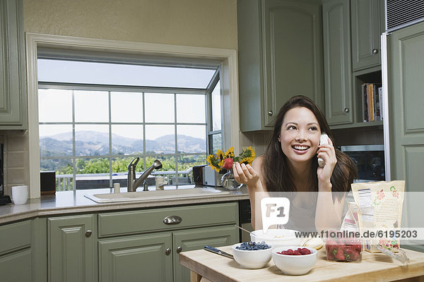 Woman eating cereal and talking on telephone in morning