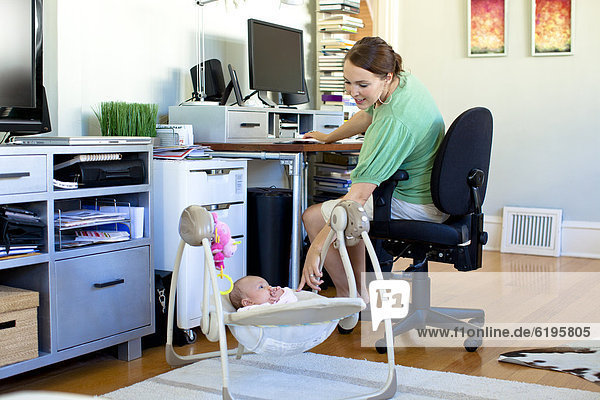 Caucasian mother working in home office with baby next to her