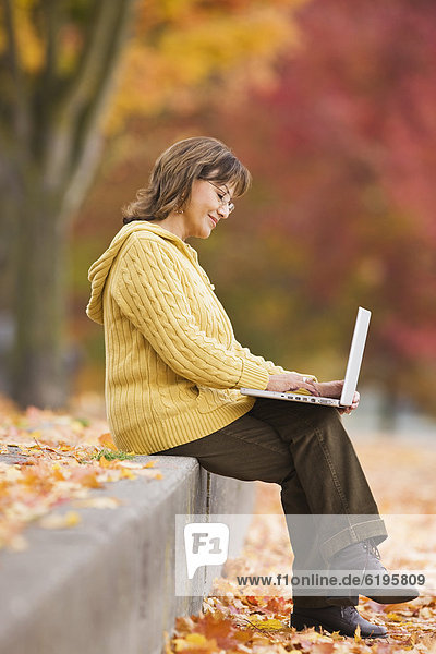 Hispanic woman using laptop outdoors in autumn
