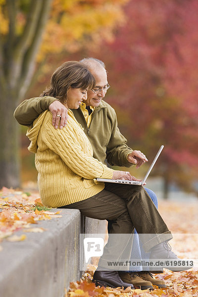 Hispanic couple using laptop outdoors in autumn