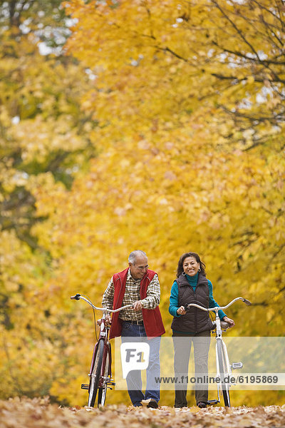 Hispanic couple walking bicycles in autumn