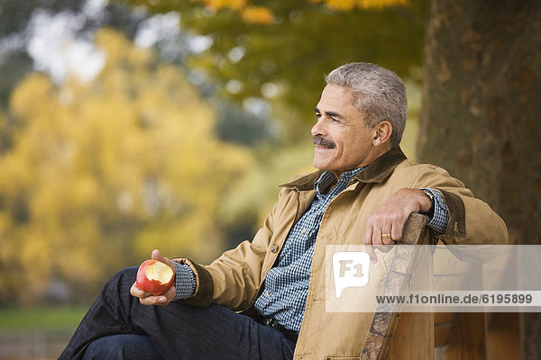 African man eating apple on park bench